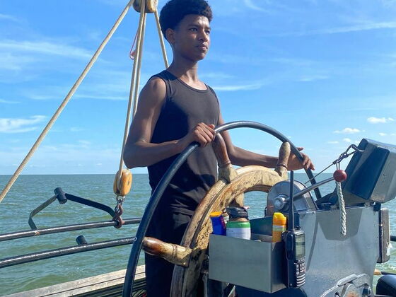 Ein Schüler hält stolz das Steuerruder des Segelschiffes fest