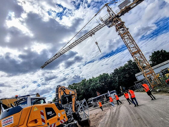 Schülergruppe laufen auf einem Kiesweg zwischen einem gelben Liebherr-Bagger und einem Kran
