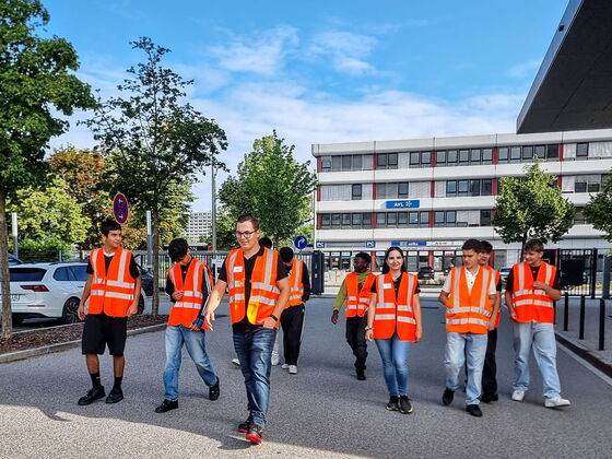 Schülergruppe in Warnwesten schreitet auf dem Firmengelände